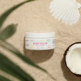 The CBDmd Botanicals CBD Sugar Body Scrub, placed in the sand alongside coconut and shells, highlighting the scrub’s natural and eco-friendly aspect